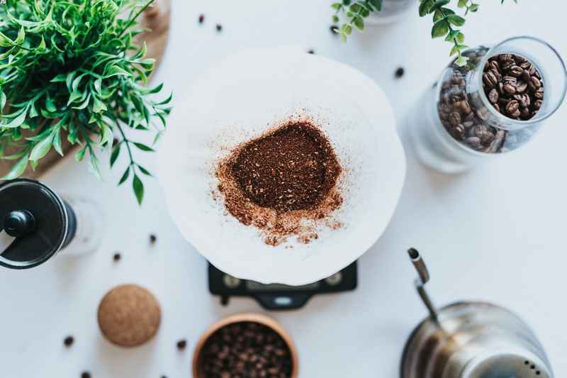 Caffè macinato all'interno di un filtro, disposto su di un tavolo con chicchi di caffè e piante.
