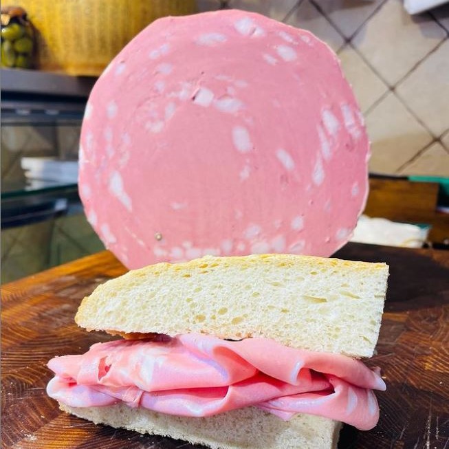 Una Mortadella Bologna con un panino alla mortadella in primo piano