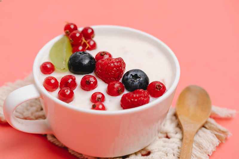 Una porzione di yogurt bianco con frutti rossi all'interno di una tazza.