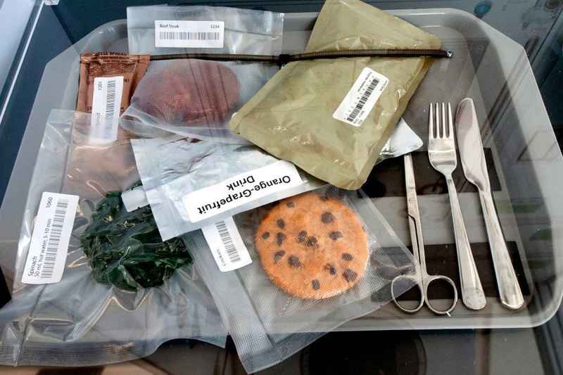 Razioni di cibo per astronauti sotto vuoto con posate in un vassoio.